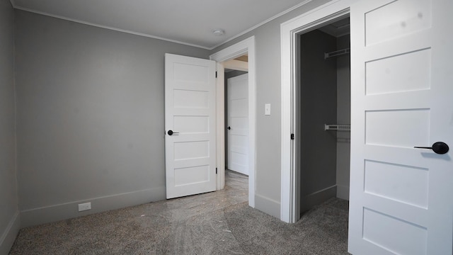 unfurnished bedroom with dark colored carpet, a walk in closet, ornamental molding, and a closet