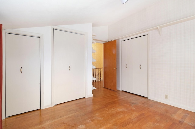 unfurnished bedroom with light wood-type flooring, two closets, and lofted ceiling