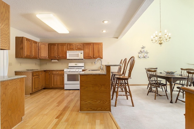 kitchen featuring pendant lighting, white appliances, sink, a textured ceiling, and light hardwood / wood-style floors