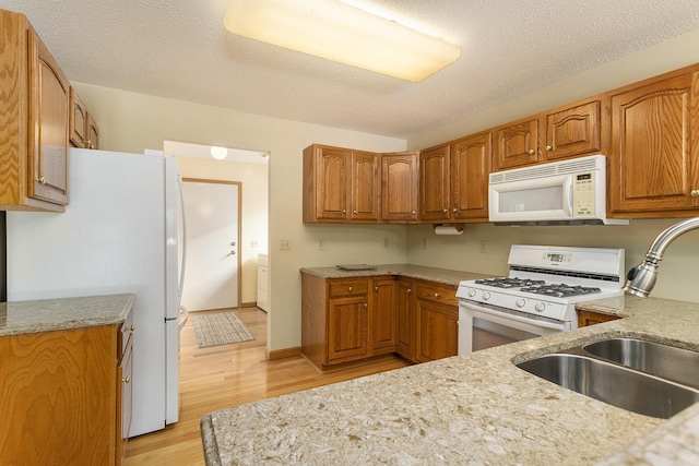 kitchen featuring a textured ceiling, white appliances, light hardwood / wood-style floors, and sink