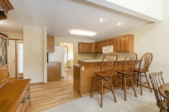 kitchen featuring kitchen peninsula, light wood-type flooring, a breakfast bar, white appliances, and a textured ceiling