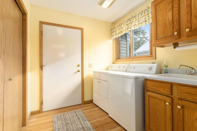 washroom with washing machine and clothes dryer, light wood-type flooring, cabinets, and sink