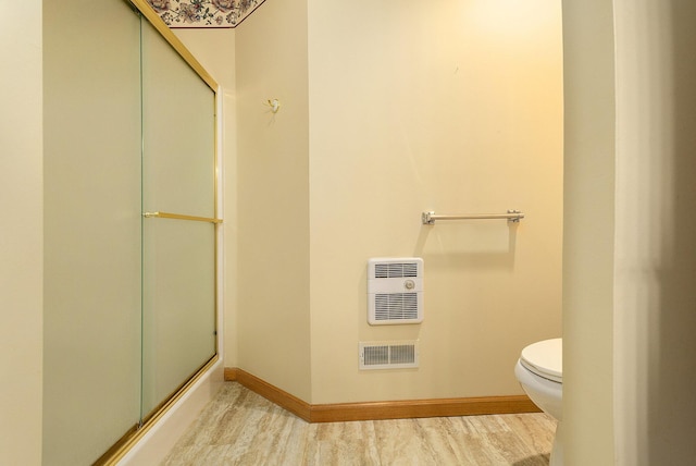 bathroom with heating unit, hardwood / wood-style floors, a shower with shower door, and toilet