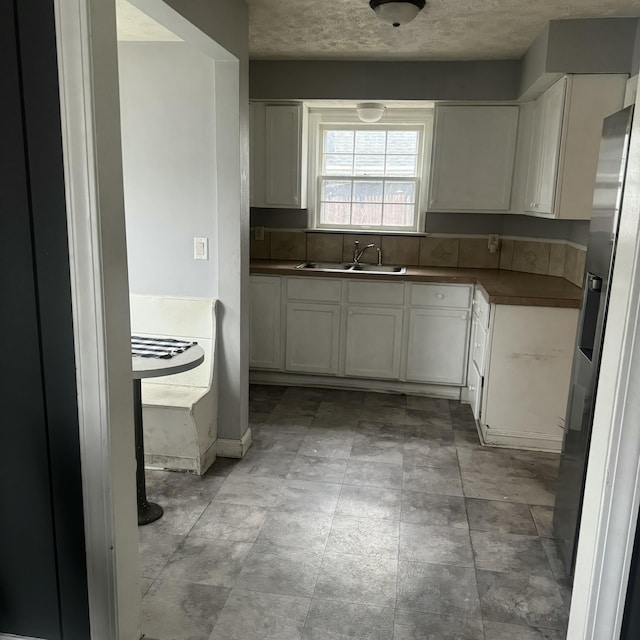 kitchen with white cabinets, stainless steel fridge, sink, and a textured ceiling