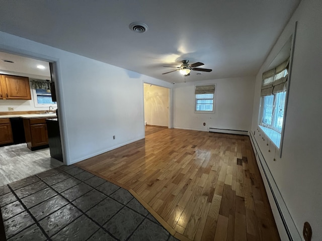 unfurnished living room featuring ceiling fan, sink, a baseboard radiator, and hardwood / wood-style flooring