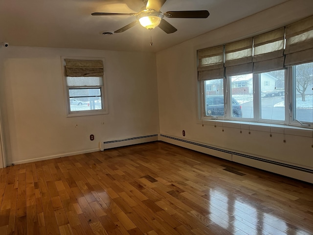 unfurnished room featuring a baseboard heating unit, light hardwood / wood-style flooring, ceiling fan, and plenty of natural light