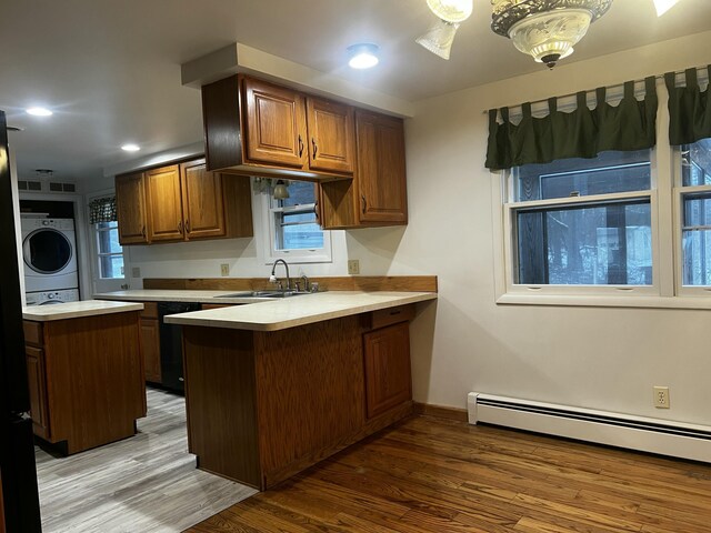 kitchen featuring stacked washer and clothes dryer, sink, light hardwood / wood-style flooring, a baseboard radiator, and kitchen peninsula