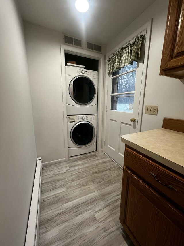 laundry room with stacked washer / drying machine, light hardwood / wood-style floors, and baseboard heating