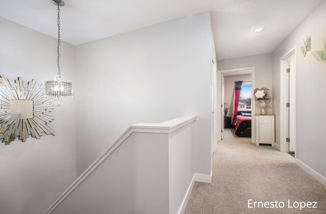 hallway featuring light carpet and a notable chandelier