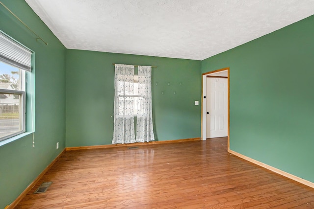 empty room with a textured ceiling and light hardwood / wood-style flooring