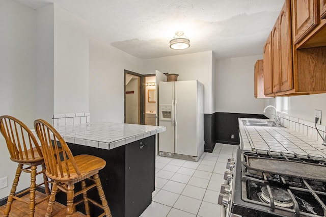 kitchen with tile counters, white fridge with ice dispenser, sink, range with two ovens, and light tile patterned floors