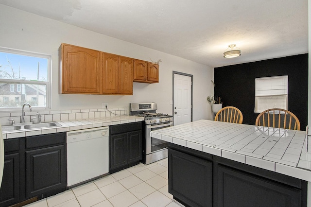 kitchen featuring sink, stainless steel range with gas cooktop, tile countertops, white dishwasher, and light tile patterned floors