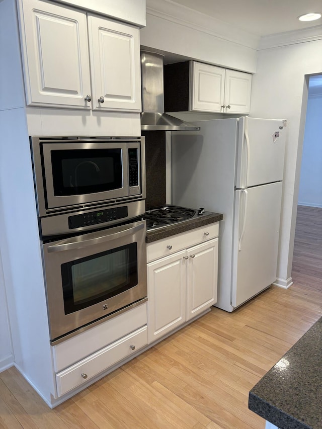 kitchen with light wood-style flooring, appliances with stainless steel finishes, ornamental molding, white cabinetry, and wall chimney range hood