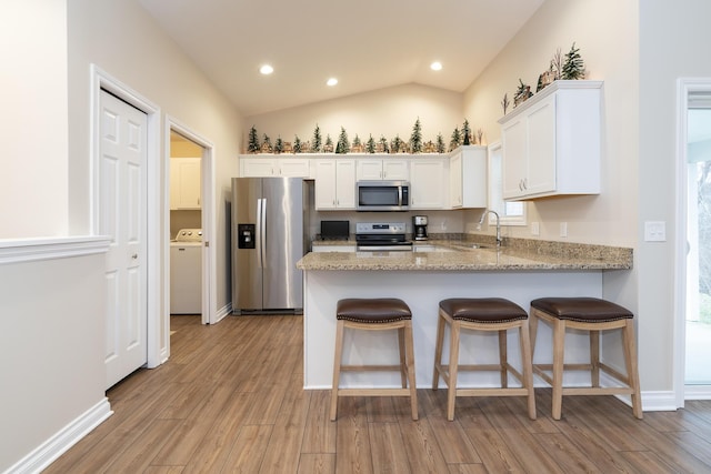 kitchen with stainless steel appliances, vaulted ceiling, sink, light hardwood / wood-style floors, and white cabinetry