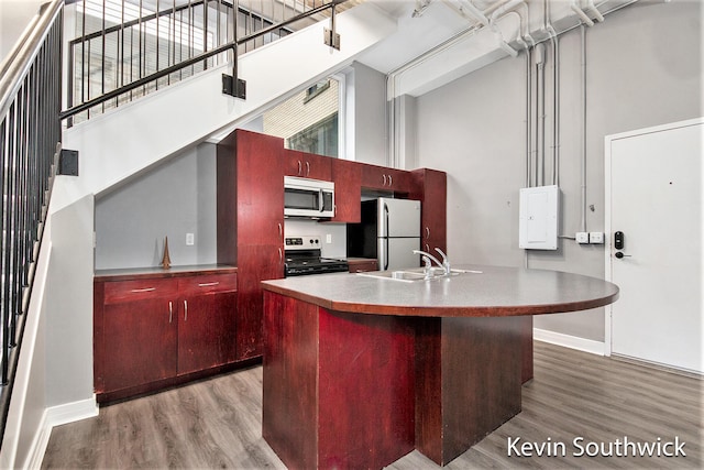 kitchen with appliances with stainless steel finishes, a kitchen island with sink, sink, wood-type flooring, and a high ceiling