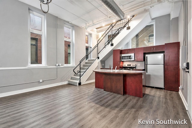 kitchen featuring a kitchen island with sink, dark hardwood / wood-style flooring, stainless steel appliances, and a high ceiling