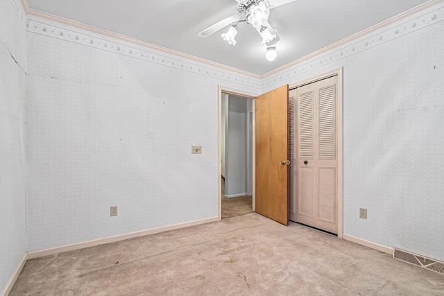 unfurnished bedroom featuring ceiling fan, crown molding, light carpet, and a closet