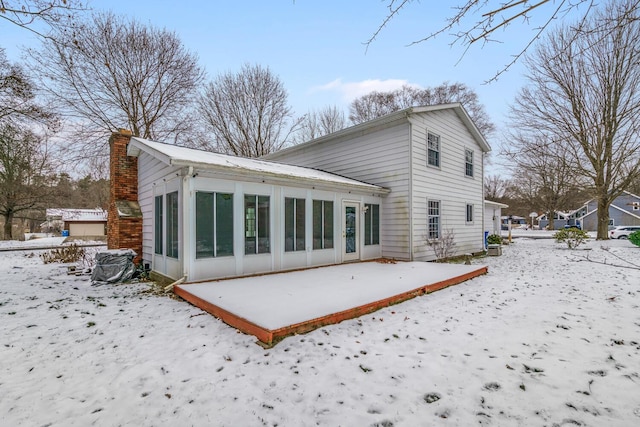 snow covered back of property with a sunroom