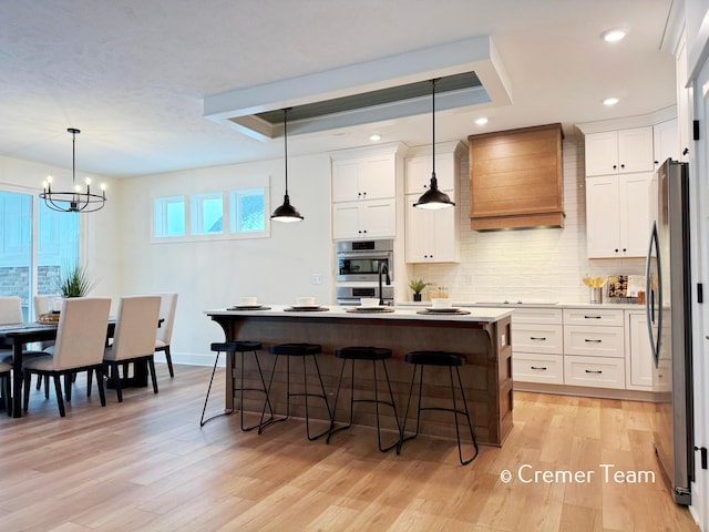 kitchen with premium range hood, light hardwood / wood-style flooring, white cabinets, and hanging light fixtures