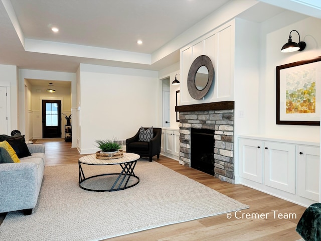 living room with light hardwood / wood-style flooring, a raised ceiling, and a fireplace