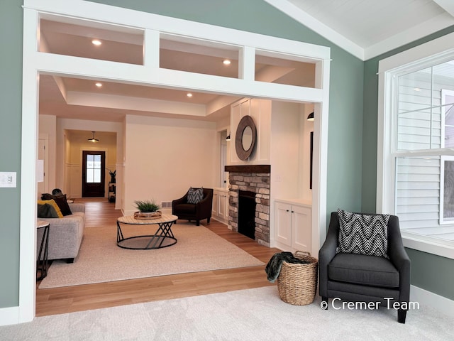 living room featuring lofted ceiling, a stone fireplace, and light wood-type flooring