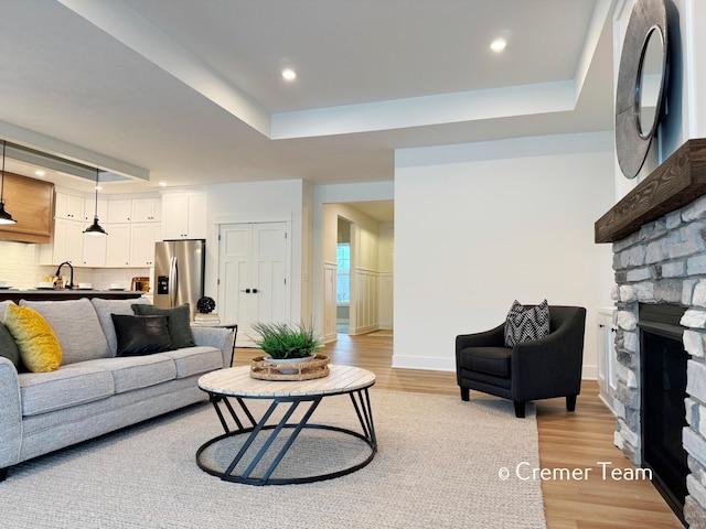 living room featuring a raised ceiling, a fireplace, sink, and light hardwood / wood-style floors