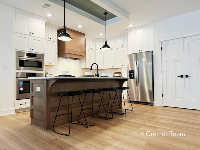 kitchen with decorative light fixtures, white cabinets, appliances with stainless steel finishes, and a kitchen island with sink