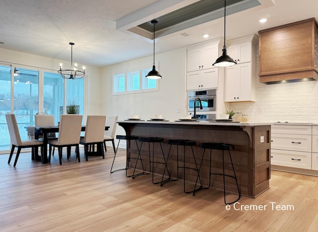 kitchen with oven, light hardwood / wood-style floors, custom exhaust hood, a center island, and white cabinets