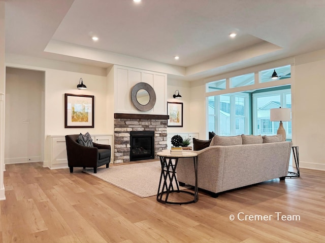 living room with light hardwood / wood-style floors, a tray ceiling, ceiling fan, and a fireplace