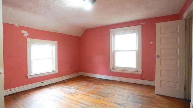 additional living space with vaulted ceiling, light hardwood / wood-style flooring, and a textured ceiling