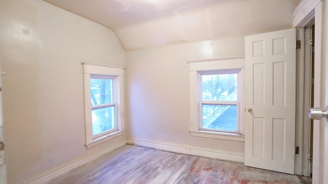 empty room with a healthy amount of sunlight, light hardwood / wood-style floors, and lofted ceiling