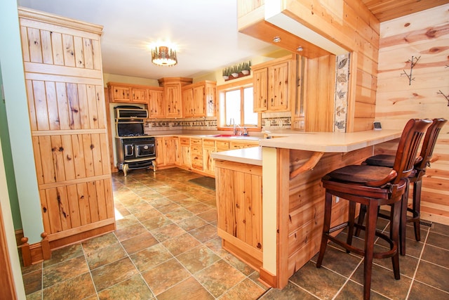 kitchen featuring light brown cabinets, a kitchen breakfast bar, sink, wooden walls, and kitchen peninsula