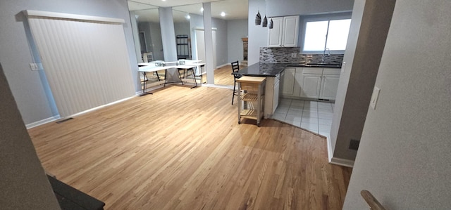 kitchen featuring decorative backsplash, light wood-type flooring, white cabinetry, and sink