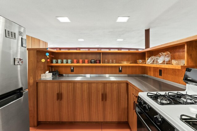 kitchen featuring white gas range oven, stainless steel refrigerator, stainless steel counters, and light tile patterned flooring