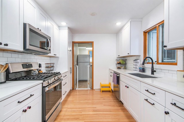 kitchen with backsplash, white cabinets, sink, light hardwood / wood-style floors, and stainless steel appliances