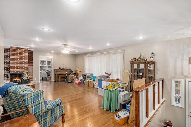 living room with ceiling fan, wood-type flooring, and a brick fireplace