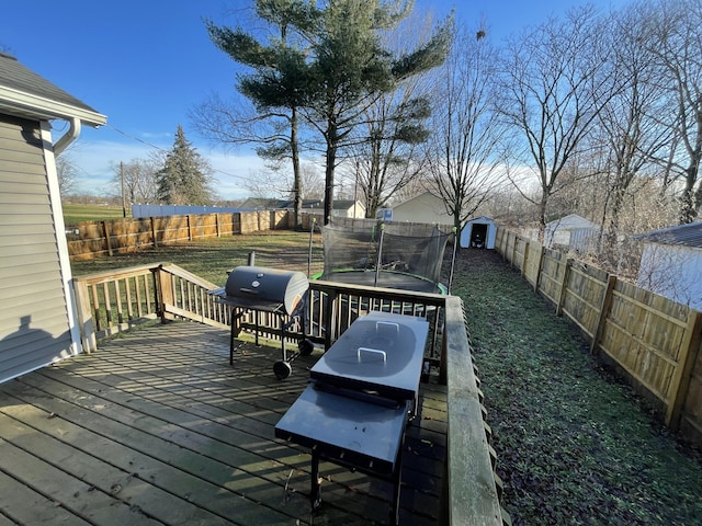 wooden deck with area for grilling, a storage unit, and a trampoline