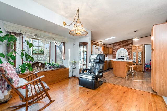 kitchen with pendant lighting, an inviting chandelier, a kitchen breakfast bar, vaulted ceiling, and light hardwood / wood-style flooring