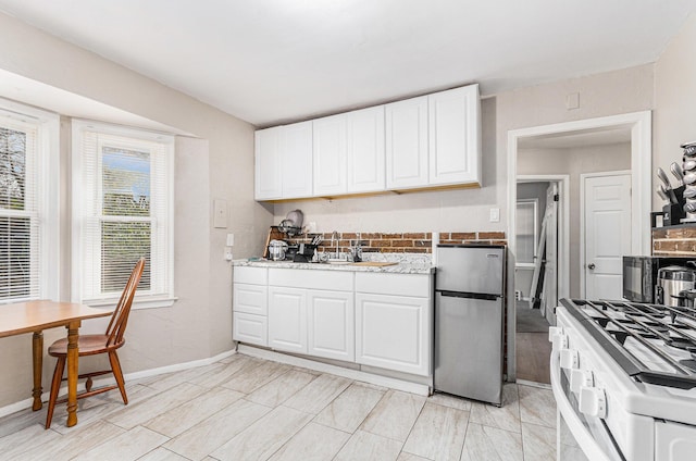 kitchen with light stone countertops, white range, sink, white cabinetry, and stainless steel refrigerator