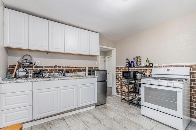 kitchen with light stone countertops, stainless steel fridge, gas range gas stove, sink, and white cabinets