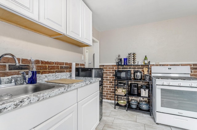 kitchen with white range with gas stovetop, light stone counters, white cabinetry, and sink