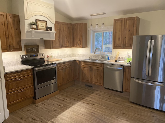 kitchen with appliances with stainless steel finishes, backsplash, sink, pendant lighting, and light hardwood / wood-style flooring