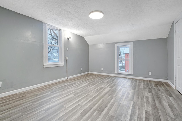 empty room with a textured ceiling, light hardwood / wood-style floors, and vaulted ceiling