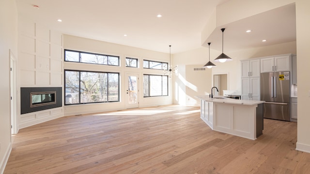 kitchen featuring sink, hanging light fixtures, stainless steel fridge, a center island with sink, and white cabinets