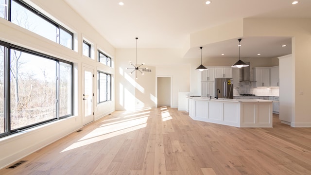 kitchen with white cabinetry, a notable chandelier, stainless steel fridge, an island with sink, and decorative light fixtures