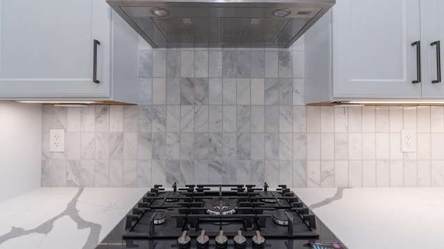 kitchen with white cabinetry, light stone countertops, wall chimney range hood, and backsplash