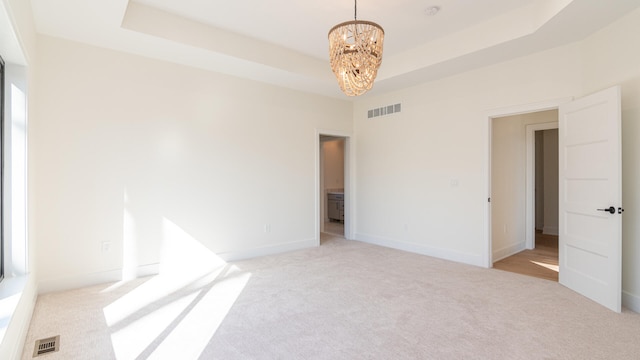 unfurnished bedroom with an inviting chandelier, light colored carpet, and a tray ceiling