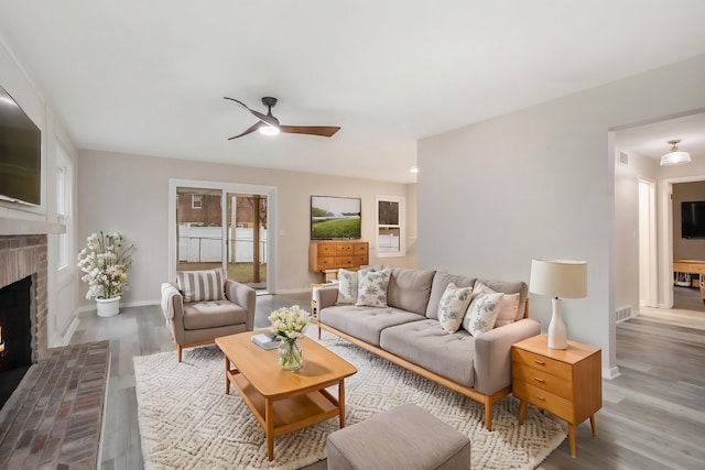 living room with ceiling fan, wood-type flooring, and a brick fireplace