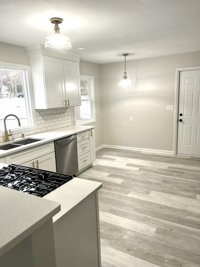 kitchen featuring stainless steel dishwasher, plenty of natural light, sink, white cabinetry, and hanging light fixtures