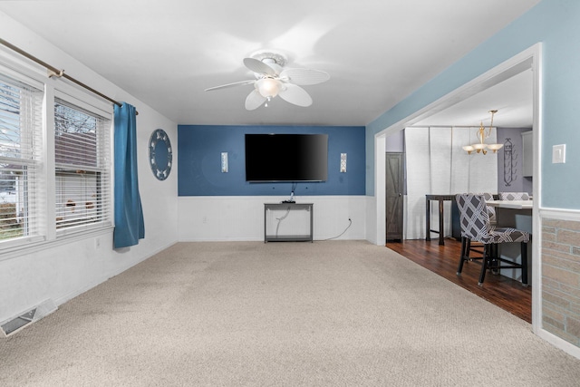 carpeted living room with ceiling fan with notable chandelier